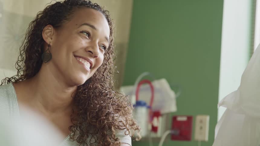 Mother smiles looking at her son laying in a hospital bed