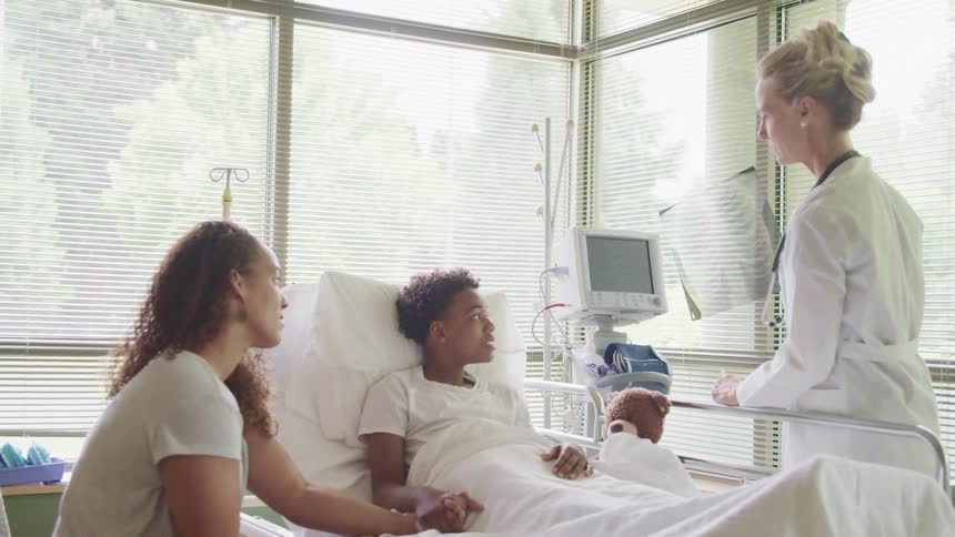 A doctor shows an x ray to a boy in a hospital bed and his mother
