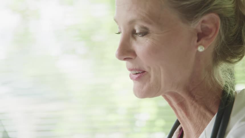 Close up of a senior female doctor wearing lab coat and stethoscope talks to a patient off screen