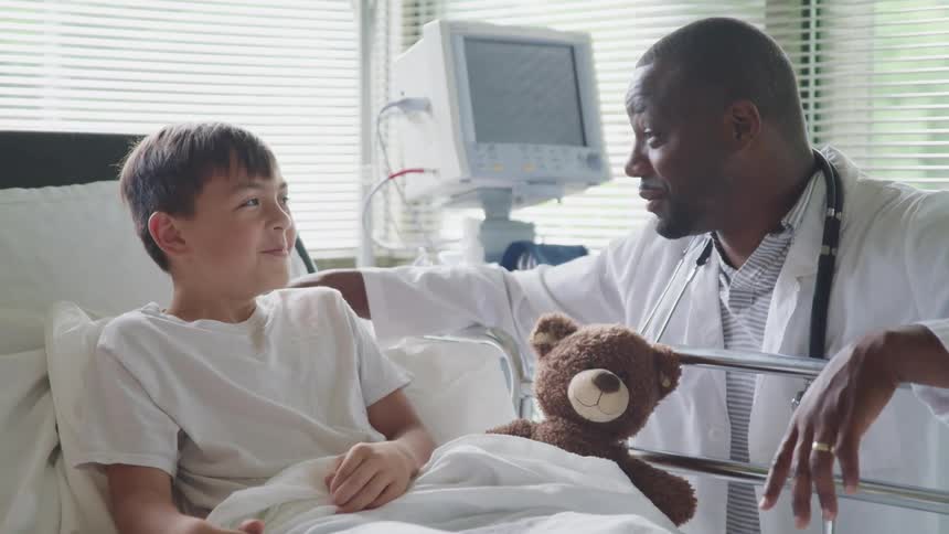 A doctor talks to a child and makes him smile while he is resting on the hospital bed