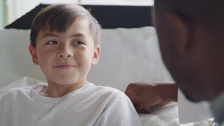 A young boy subtly smiles while shaking his head and listening to an adult male