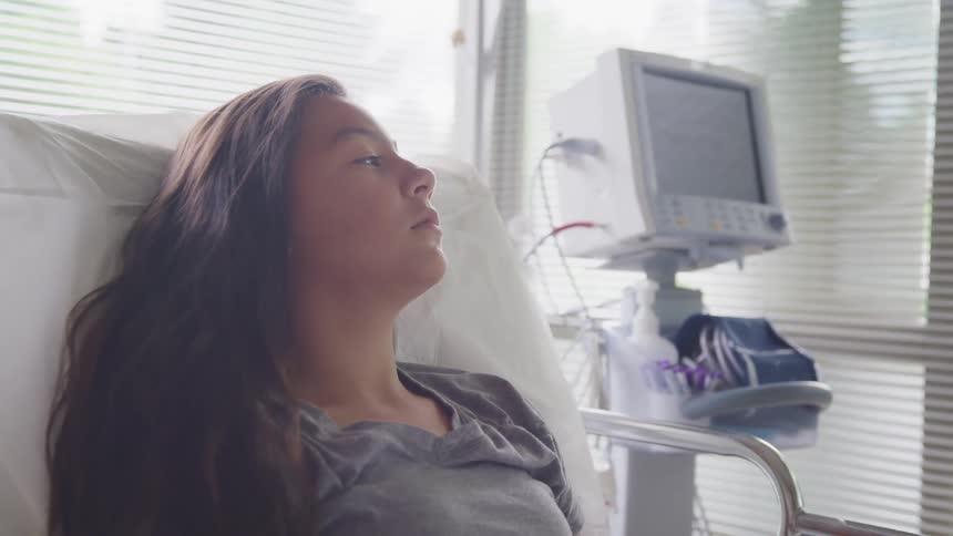 A girl lays in a hospital bed looking out the window