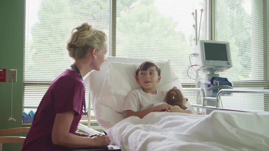 Nurse sits at young patients bedside talking to him