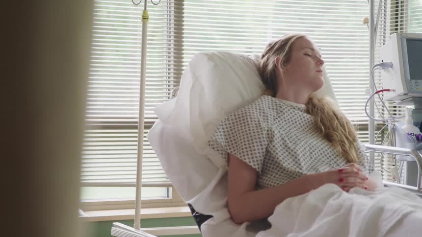 A woman sleeps in a hospital bed on the ground floor of a hospital