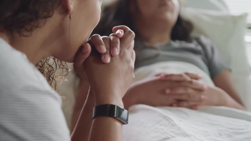 A woman with a wristwatch sitting by the bedside of another woman