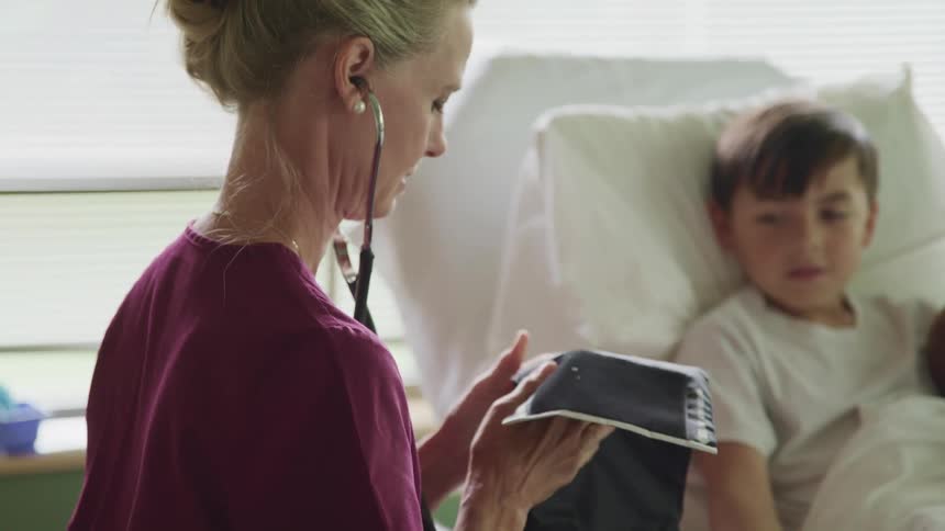 A female nurse prepares a blood pressure cuff for a child patient in a hospital bed