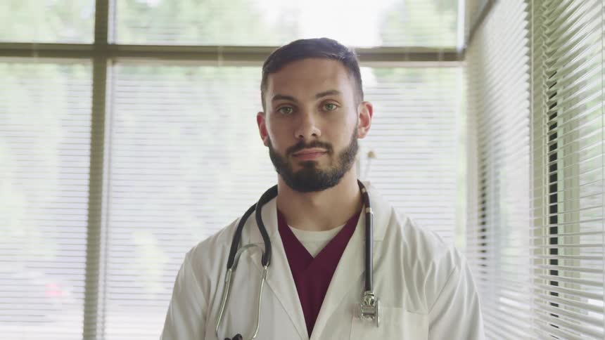 Doctor with a beard and a stethoscope around his neck faces the camera with eye contact in the clinic