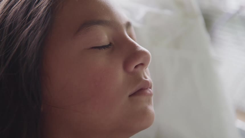 A young girl lying in bed at home closes her eyes