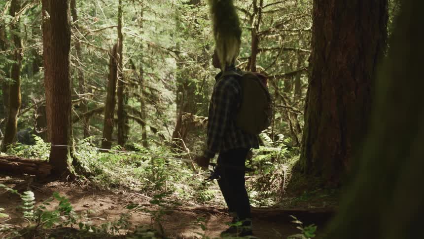 A teenage boy carrying a fishing rod walks through a forest