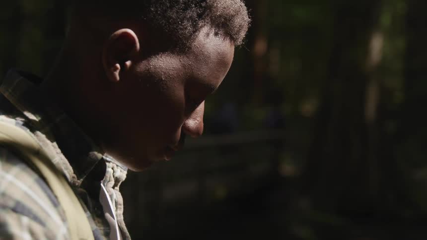 Side view of a young black man looking down in the forest