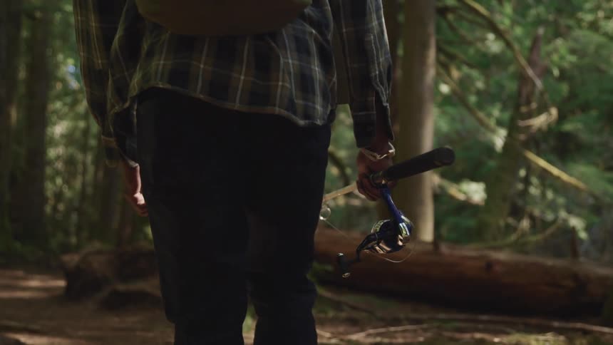 A person walking in the woods carrying a fishing pole