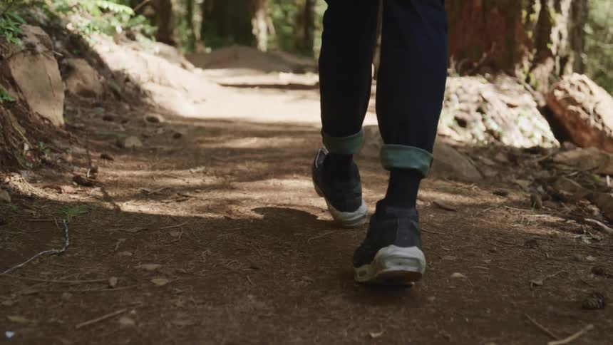 Man with jeans and a pair of black shoes walks along a dirt track in the forest
