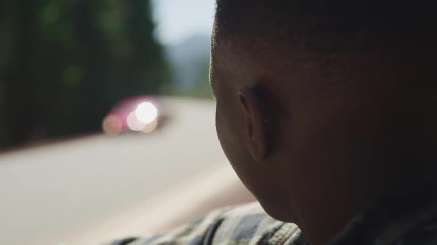 Side view of a young black man watching a red car passing by