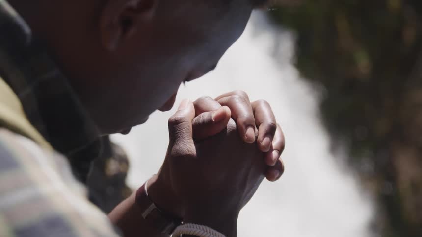 A young man prays as the sits next to a waterfall