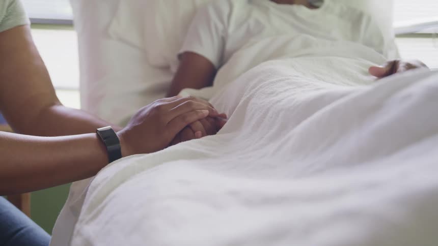 Mother holds the hand of her son lying in a bed in the hospital