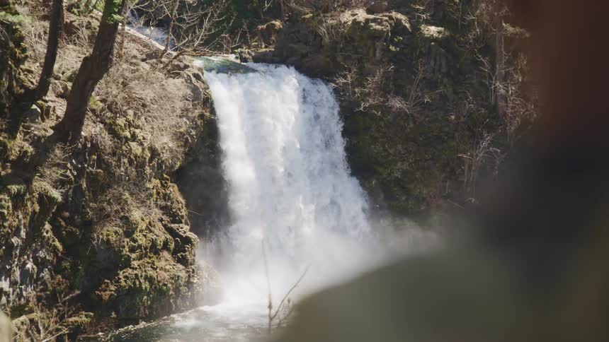 Teenage black boy watches a waterfall cascading from the rocks above
