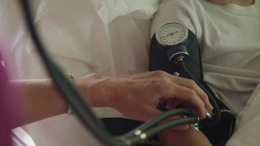 A person with a stethoscope and scrubs taking a patients blood pressure and listening to their pulse