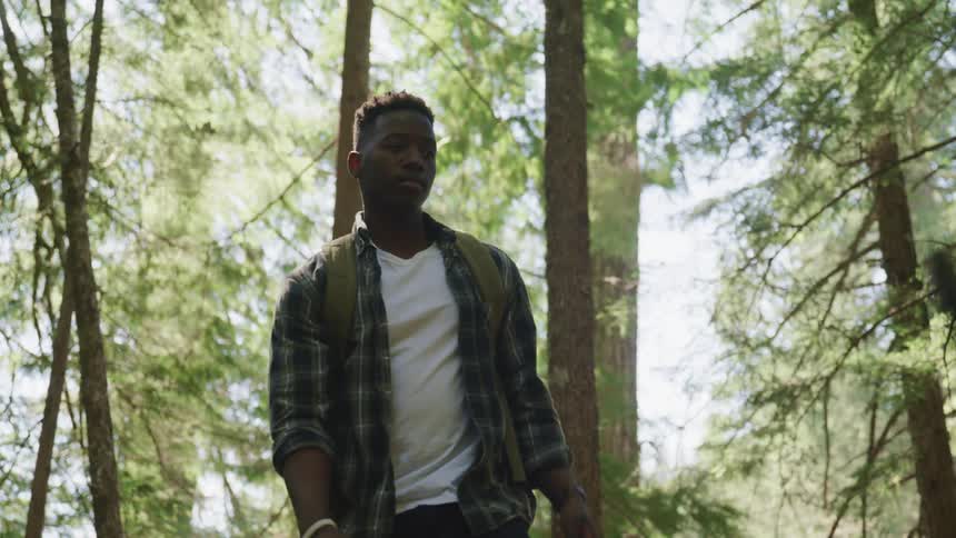 Black young man with a shirt and a backpack walks in the woods