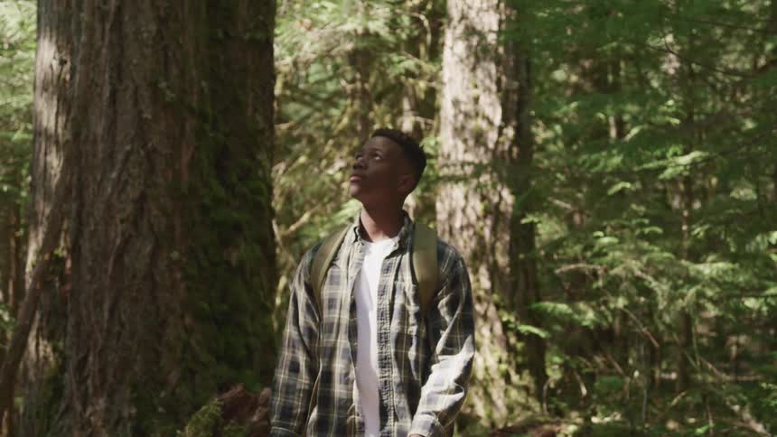 Teenage black boy with a shirt and a backpack walks on dirt track in the forest