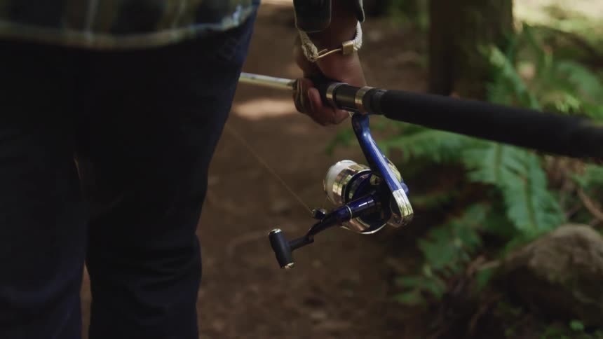 A man walking through a wooded area carrying a fishing rod
