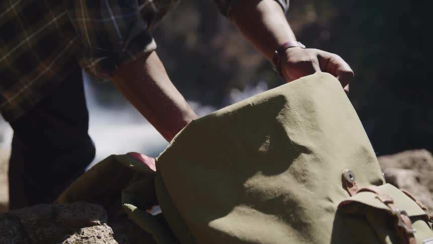 A photographer retrieves his camera from his bag and prepares to take a photograph of a waterfall