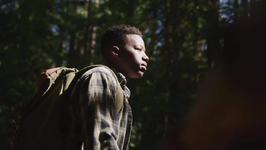 A boy with a backpack standing with trees and the sky in the background