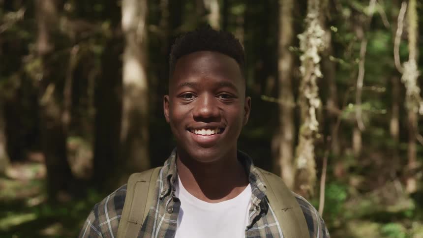 Young man hiking in the forest looks at the camera smiling