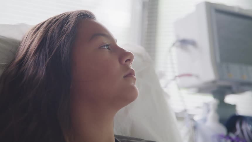 A girl rests in a hospital bed while lost in thought