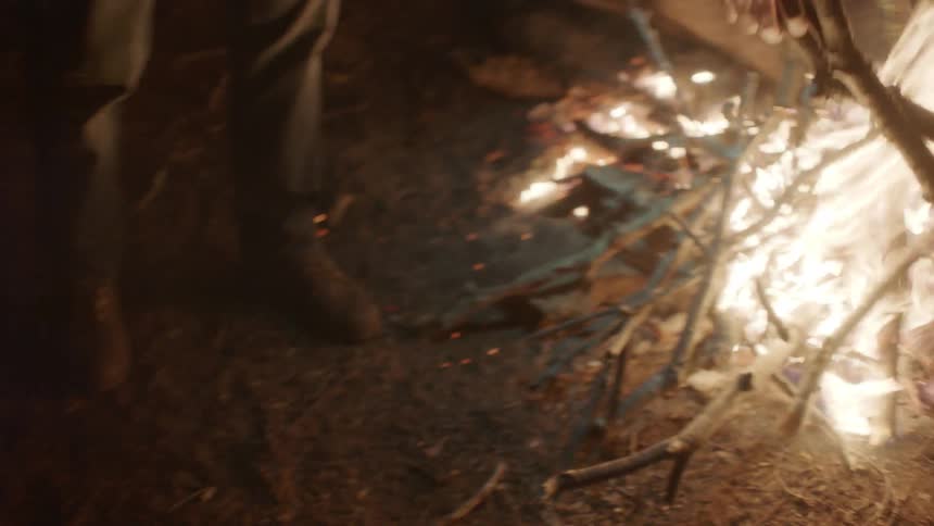 A man throws sticks on a campfire