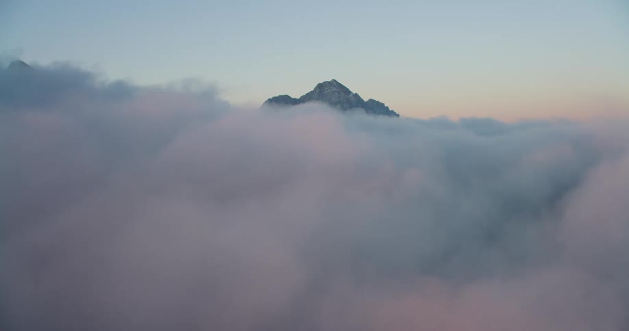 An aerial view of a mountain peak poking out from fluffy clouds