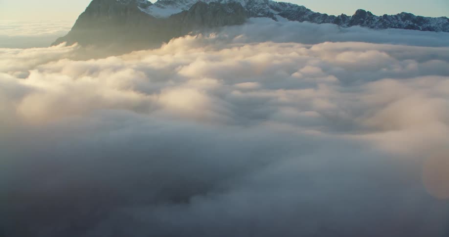 Aerial view of a snow covered mountain range over the clouds at sunset