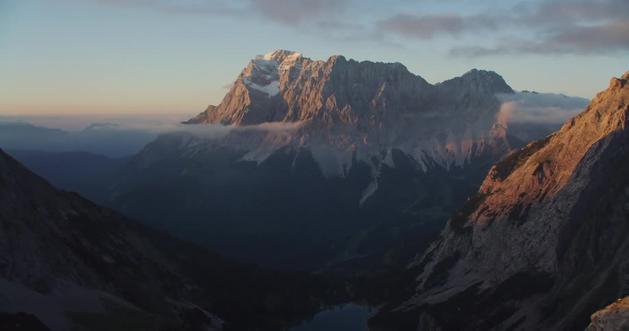 An aerial view of tall mountains with snow at sunrise
