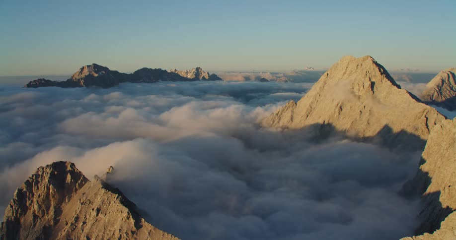 An aerial view of mountains poking through clouds at dawn