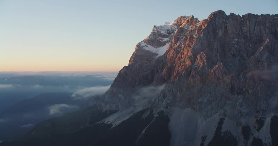 Aerial view of the snow covered peak of a mountain range over the clouds at sunset