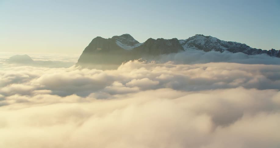 Aerial view of the snow covered peaks of a mountain range over the clouds at sunset