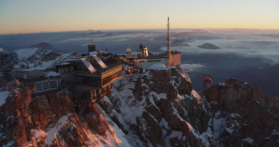 An aerial view a building on a snowy mountain peak at sunset