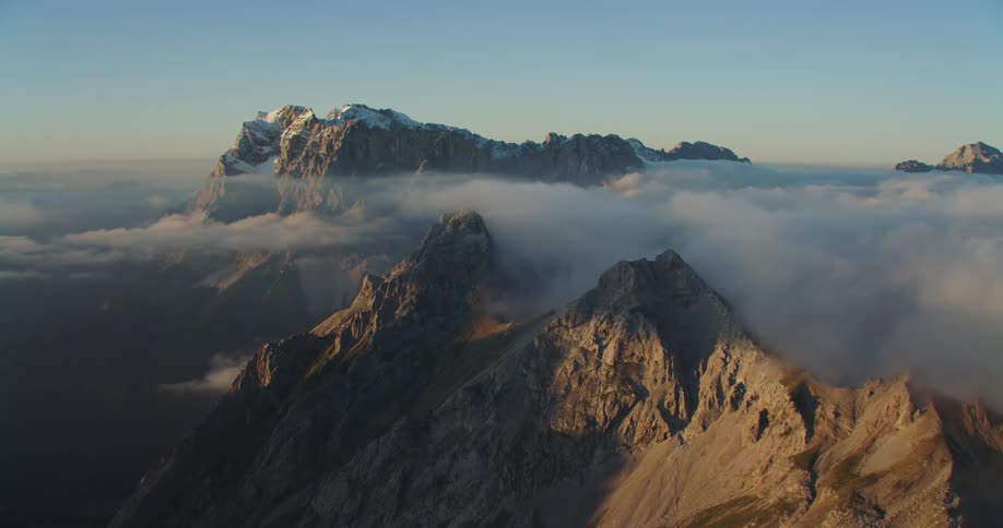 Aerial view of snow covered peaks of a mountain range over the clouds at sunset