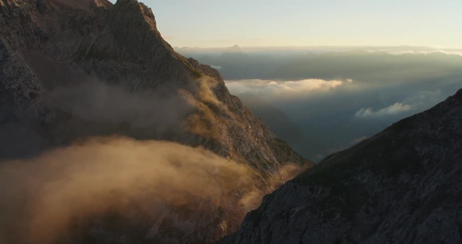 Aerial footage goes through mountains to reveal a valley with a lake below at sunrise