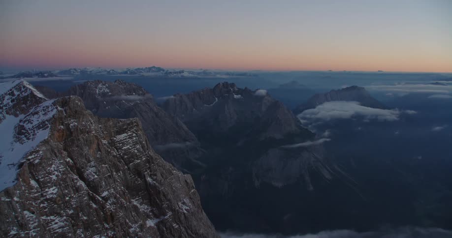 Aerial view of the snow covered peaks of a mountain range over the clouds at sunset