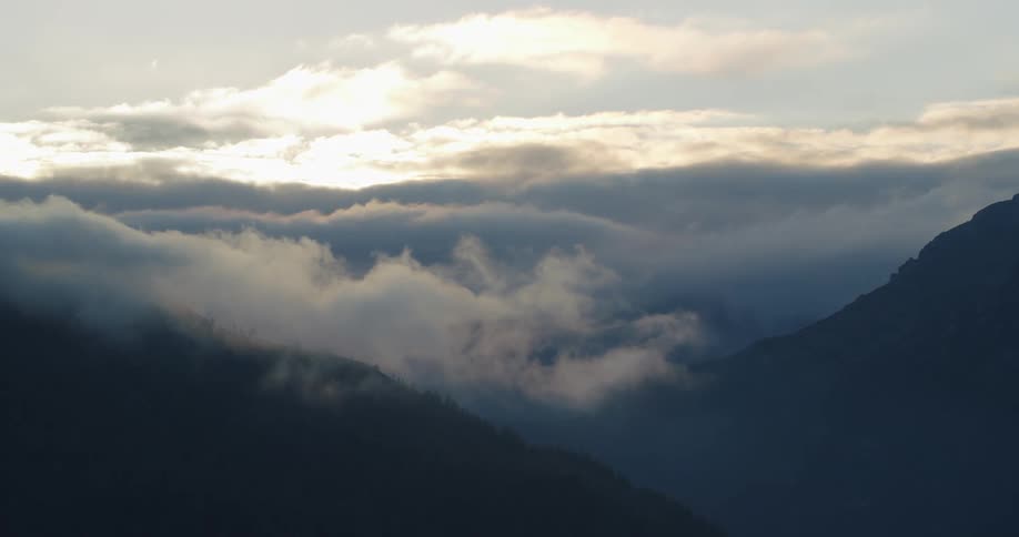 An aerial view of a mountain is displayed surrounded by clouds