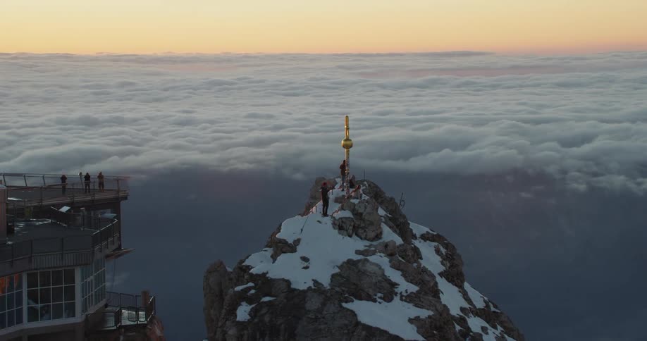 An aerial view of a mountain covered in snow is displayed while the sun is setting