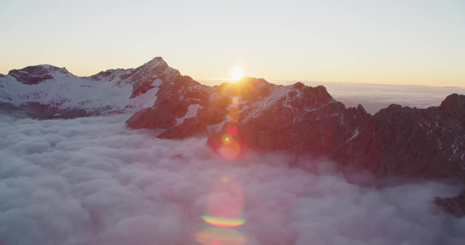 The sun setting over the top of mountains surrounded by clouds