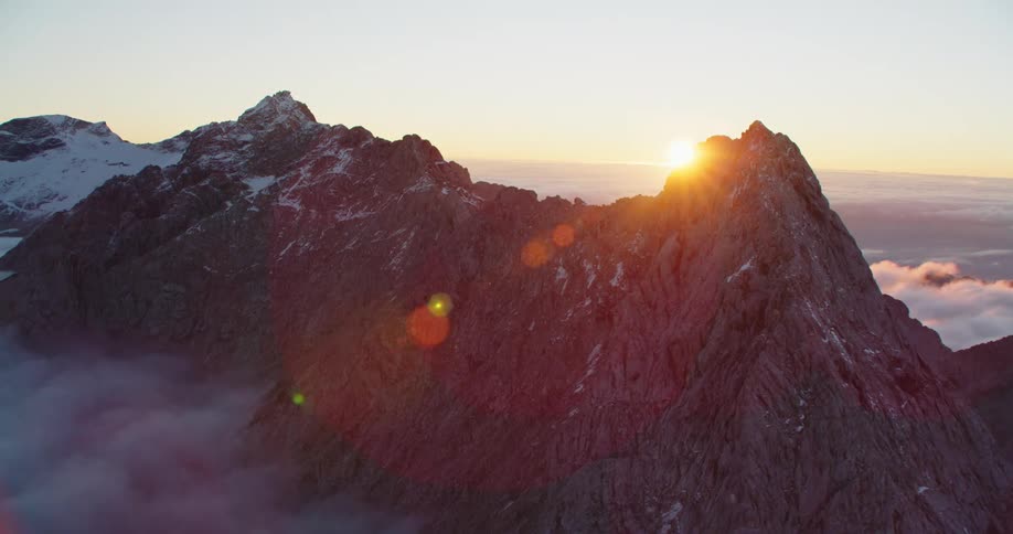 Aerial view of snow covered mountain range peaks over the clouds at sunset
