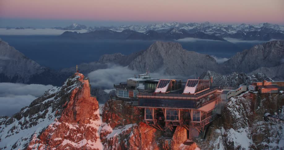 A man and woman stand at a cross on a mountain top next to an observatory