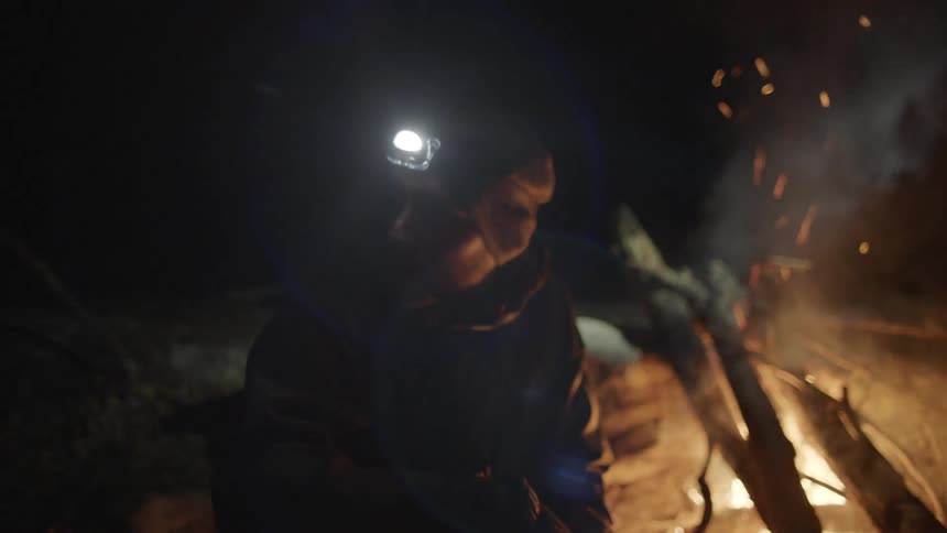 A man is sitting near a campfire at night