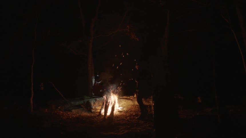 A man wearing a headlamp walks near a campfire
