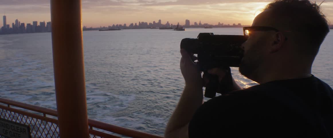 A man films from a boat near sunset