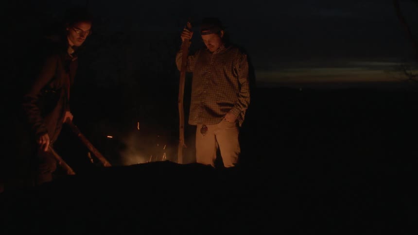 Men stand around a campfire at night