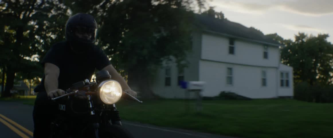 A person drives a motorcycle down a road at sunset