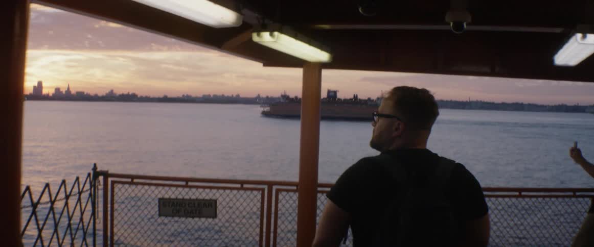 A man walks towards the rear of a boat with a cityscape in the distance
